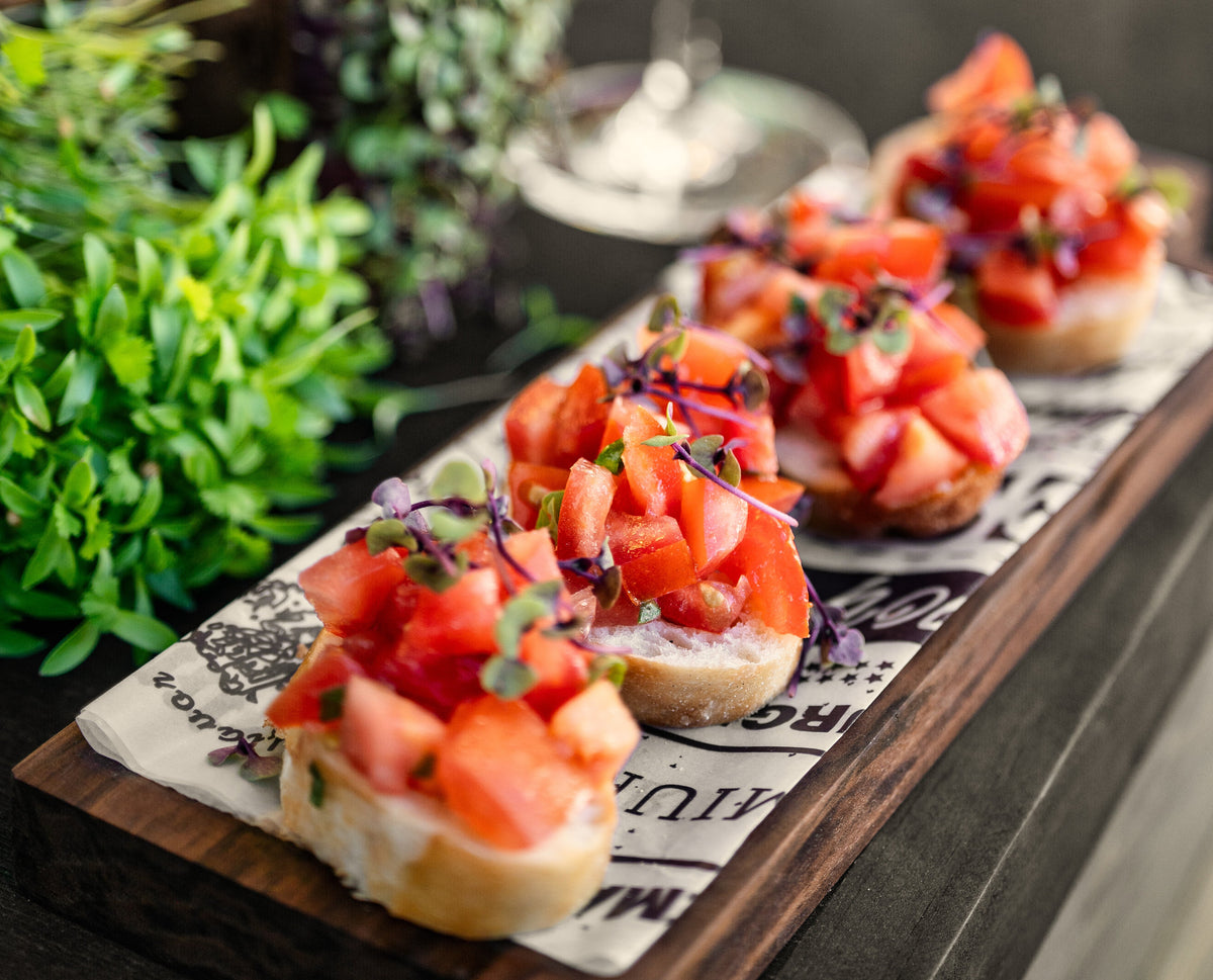 Tomato bruschetta topped with fresh herbs and microgreens, served on a wooden board.